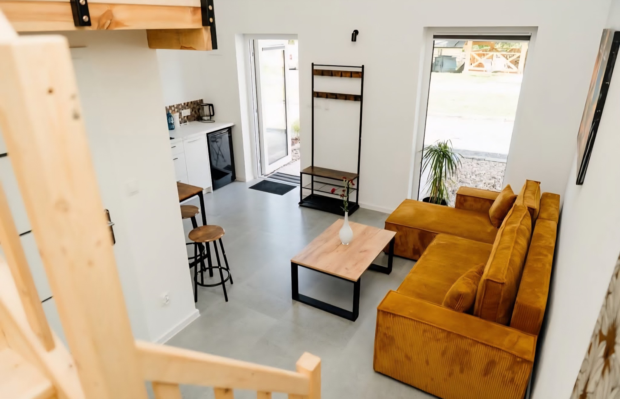 Jasne wnętrze z antresolą: salon z musztardową sofą, drewnianym stolikiem i schodami. Widok z góry podkreśla przestronność i nowoczesny design. Minimalistyczny wystrój.