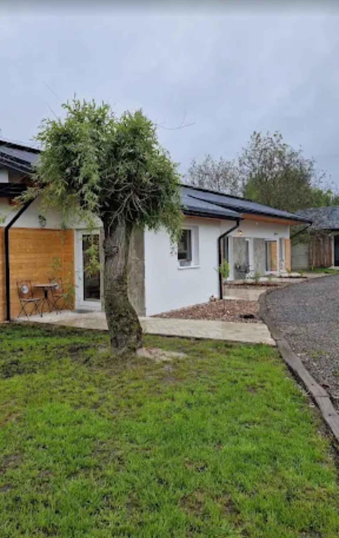 Nowoczesny dom parterowy z białymi ścianami i drewnianą elewacją, widok z zewnątrz, z zielonym trawnikiem i drzewem na pierwszym planie. Minimalistyczny design.