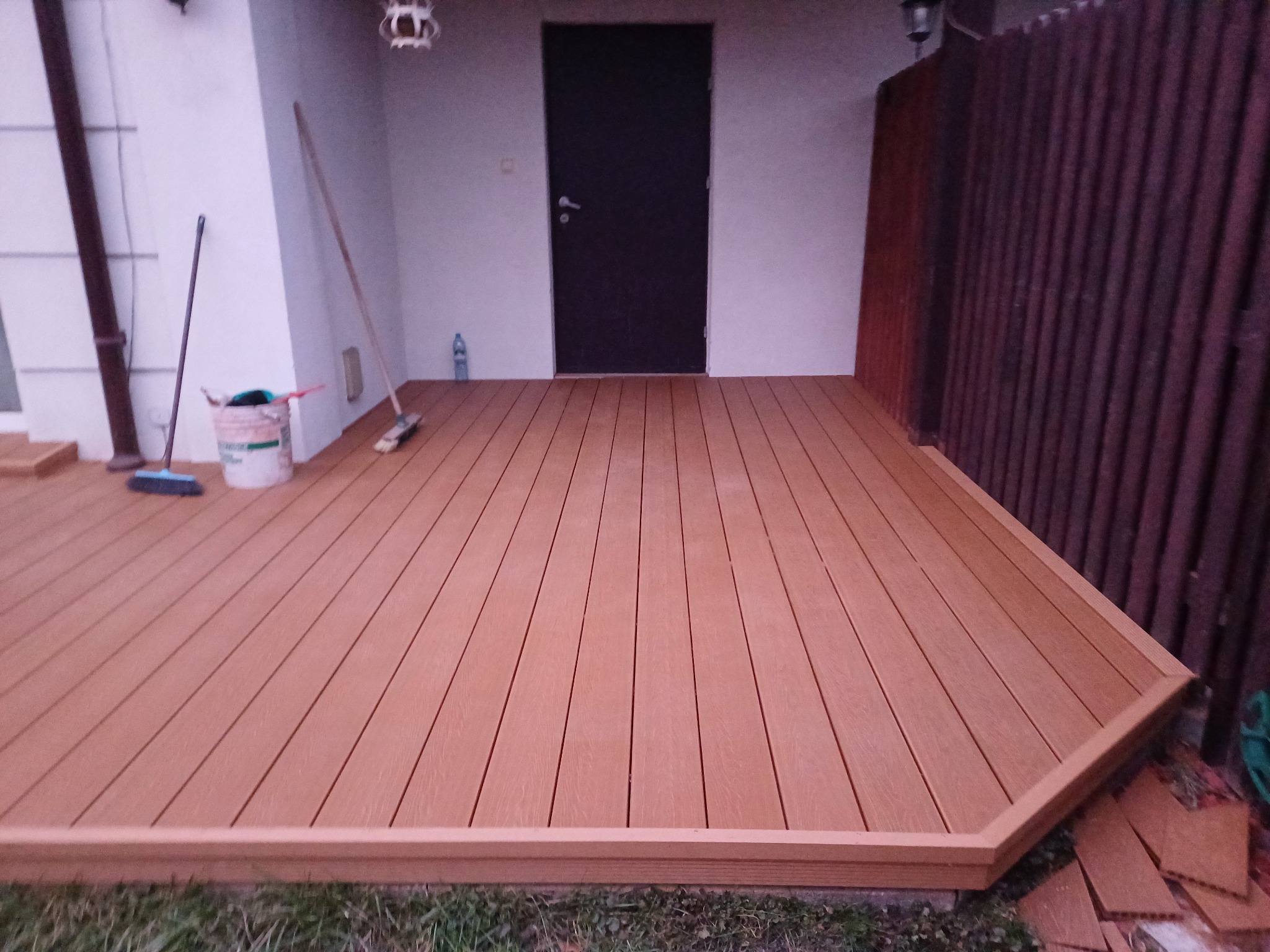 Nowo wybudowany taras z desek kompozytowych, widok z poziomu gruntu na narożnik, z widocznymi narzędziami i resztkami materiałów po budowie.