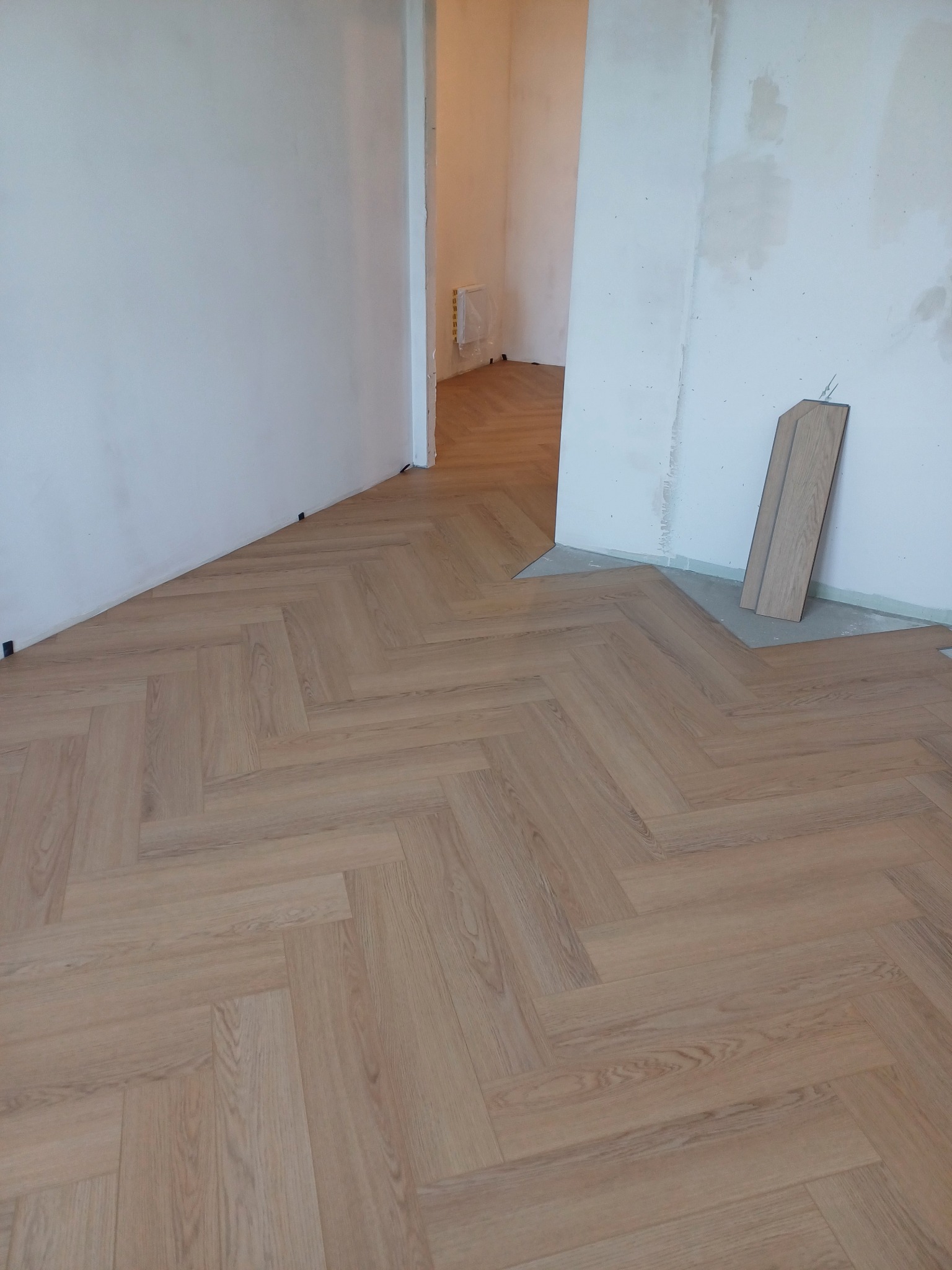 Jodełka francuska ułożona z paneli podłogowych w jasnym odcieniu drewna, widoczne niedokończone ściany i przygotowane panele do dalszego montażu.