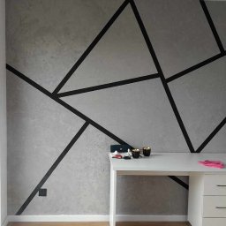 Ekskluzywne ściany - Ściana z szarym tynkiem dekoracyjnym i geometrycznymi czarnymi liniami, białe biurko z akcesoriami i białe drzwi z poziomymi przeszkleniami.