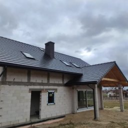 Dachiman - Dom w trakcie budowy z nowym, ciemnoszarym pokryciem dachowym z dachówki ceramicznej, widoczne okna dachowe i czarny komin, zamontowane rynny, ściany z białego bloczka.