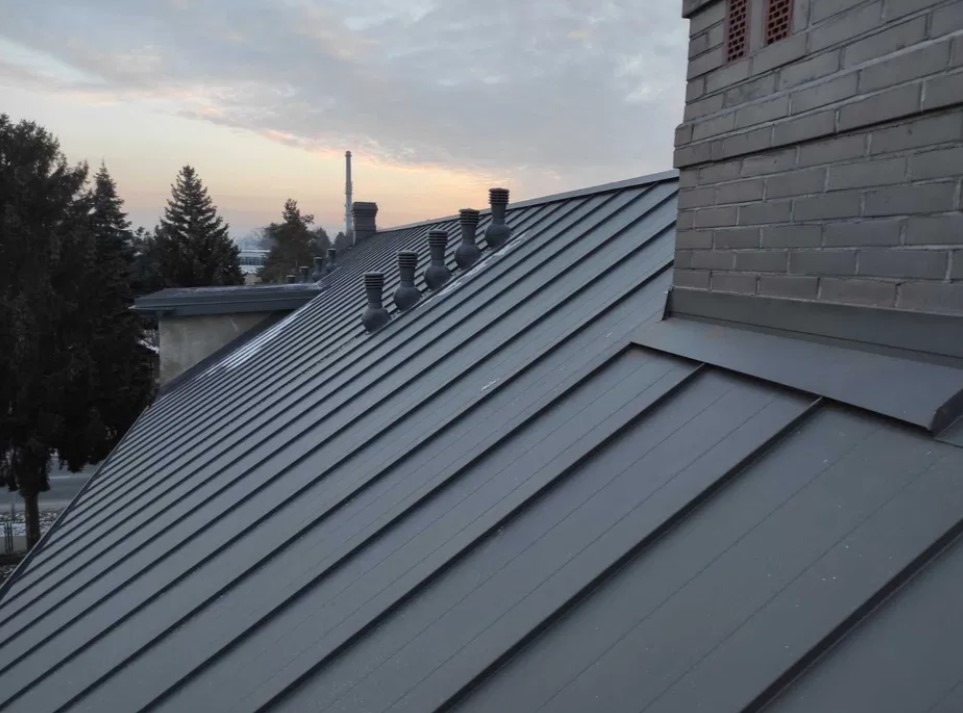 Szary, metalowy dach z kominem i kilkoma odpowietrznikami w Lublinie, widziany pod kątem w pochmurny dzień.