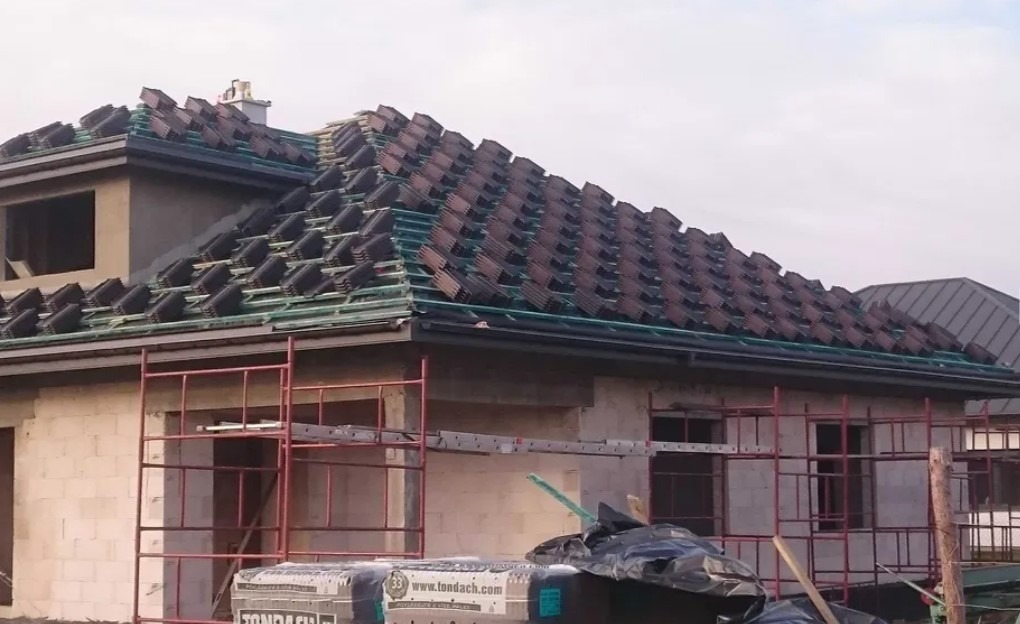 Dom w trakcie budowy, z przygotowaną konstrukcją i częściowo ułożoną dachówką ceramiczną marki Tondach, widoczne rusztowania.