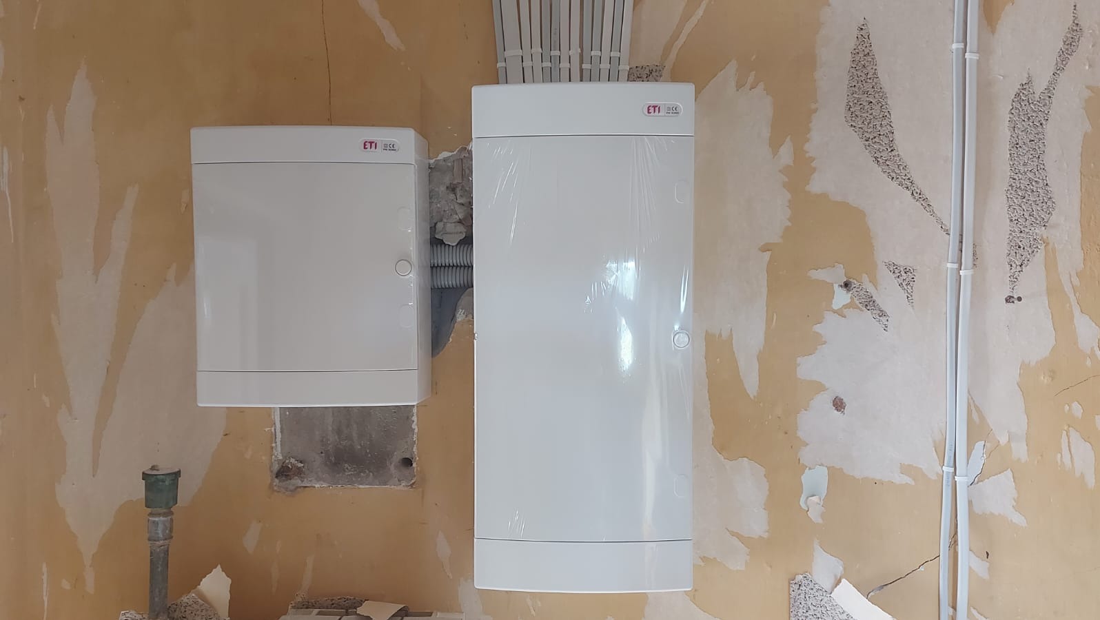 Dwie białe skrzynki elektryczne marki ETI zamontowane na ścianie w trakcie remontu w Międzyrzecu Podlaskim, widoczne przewody elektryczne w peszlu i rurkach PCV.
