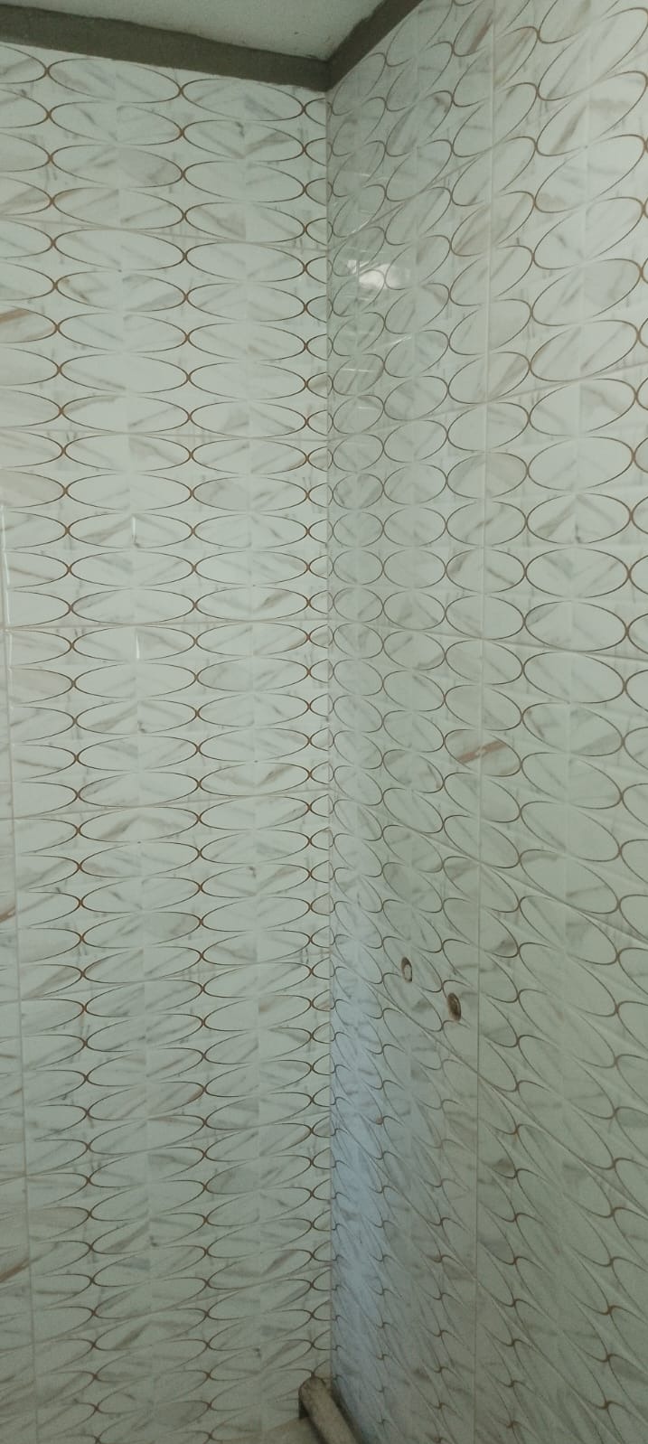 Wykończona ściana w łazience z białymi, wzorzystymi płytkami ceramicznymi układanymi w rzędach, widoczne fugi i narożnik ściany.