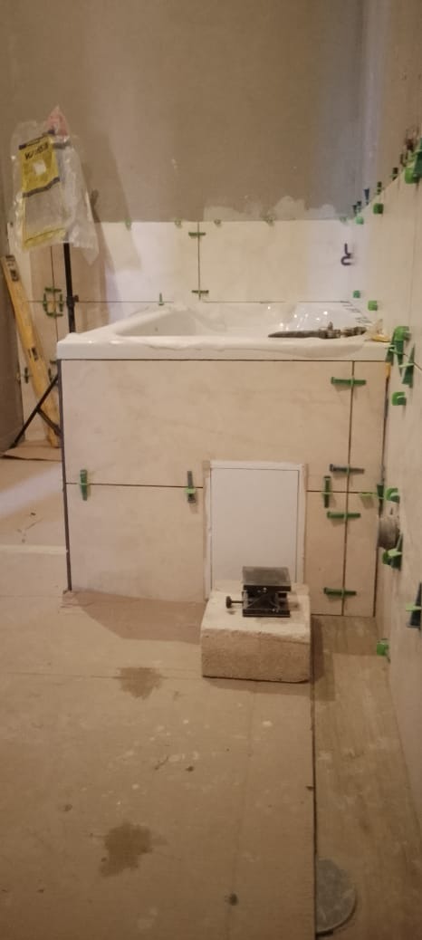 Montaż płytek wokół wanny w Legnicy, z użyciem krzyżyków dystansowych i poziomicy, widoczny otwór rewizyjny i podnośnik do płytek na bloczku.