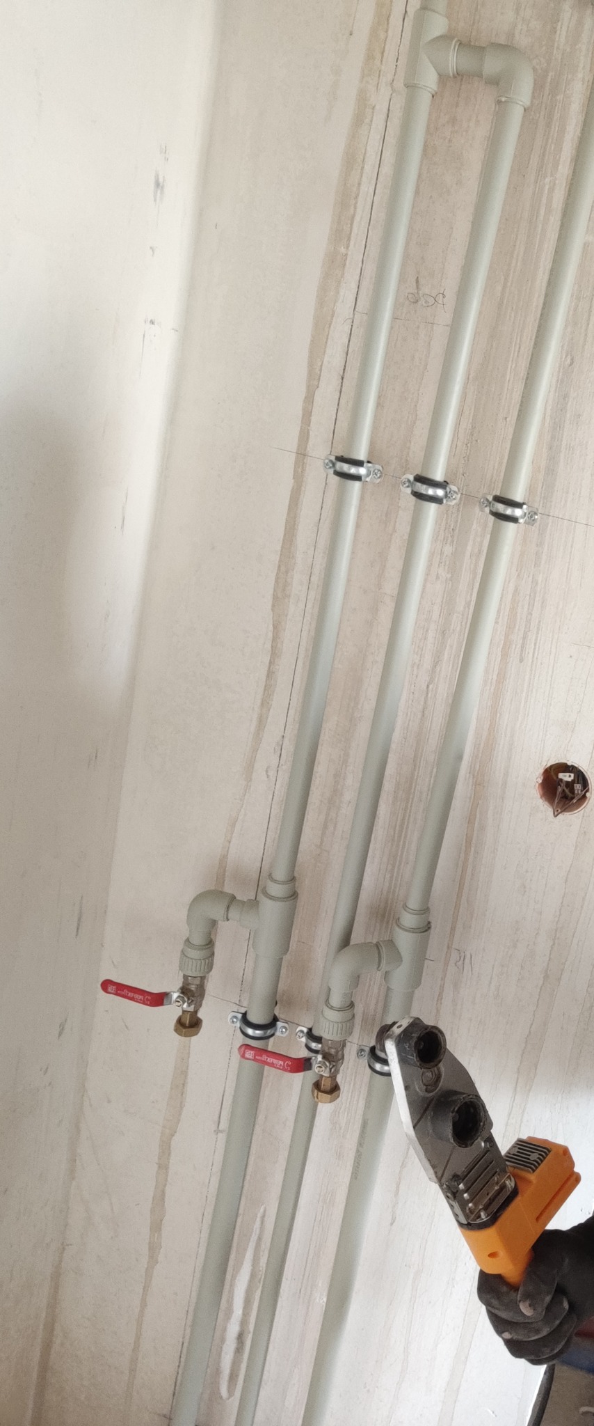 Montaż instalacji wodnej z rur PP za pomocą zgrzewarki, widoczne zawory kulowe i uchwyty mocujące do ściany w surowym stanie.