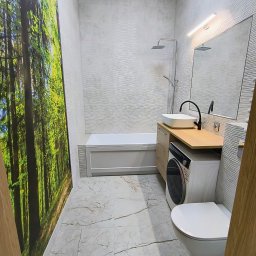 Patrycja Matuszewska P&P Art-Bud - Nowoczesna łazienka z fototapetą leśną, umywalką nablatową na drewnianym blacie, pralką pod blatem i wiszącą toaletą; płytki imitujące fale na ścianach i marmurowe na podłodze.