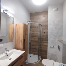 Patrycja Matuszewska P&P Art-Bud - Nowoczesna łazienka z kabiną prysznicową narożną, umywalką z szafką z drewnianymi frontami, toaletą i pralką, wykończona płytkami w odcieniach bieli i drewna.