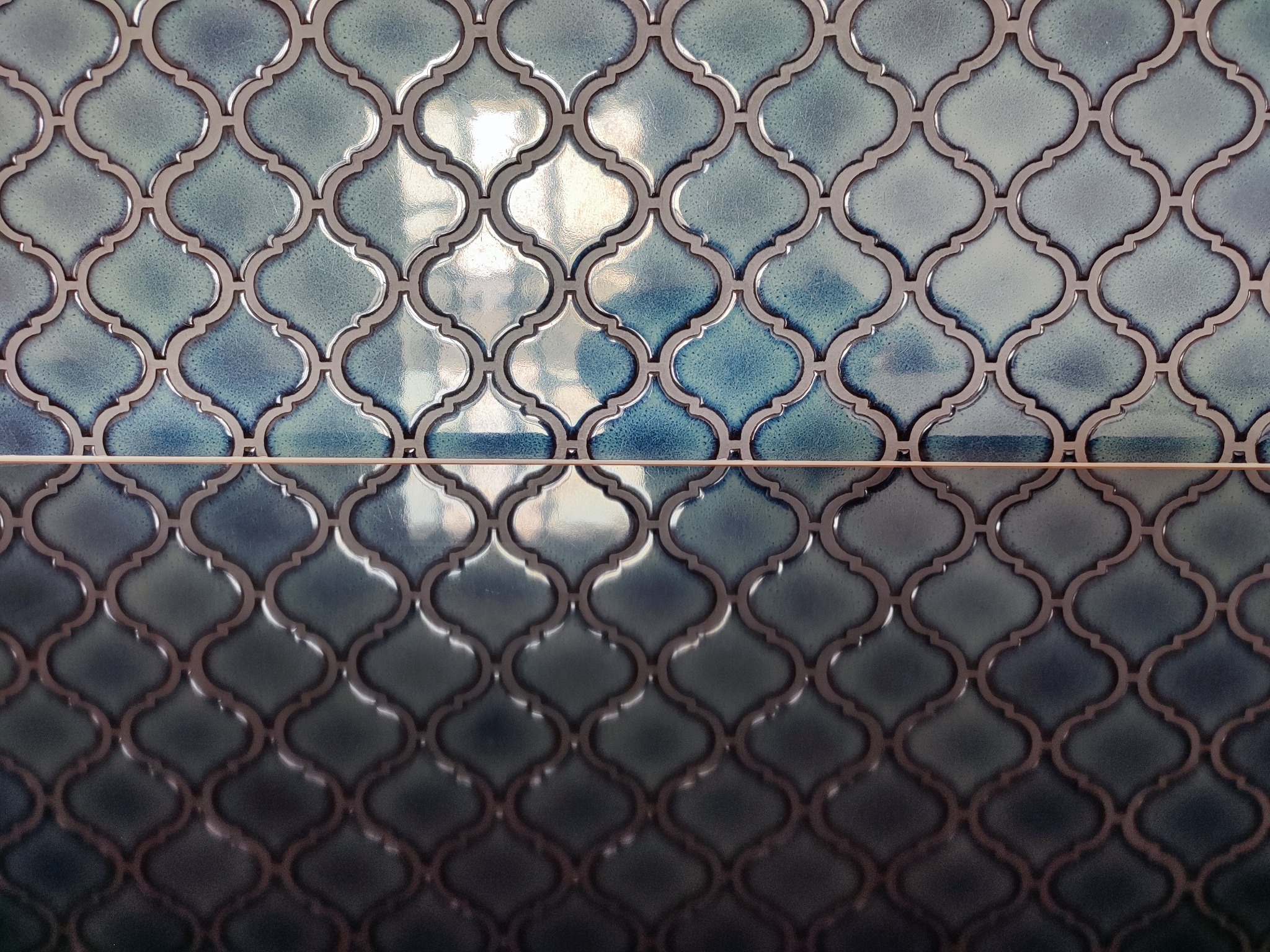 Błyszcząca, dekoracyjna mozaika ścienna w odcieniach błękitu i granatu z motywem marokańskim, ułożona w równe rzędy, z widoczną fugą.