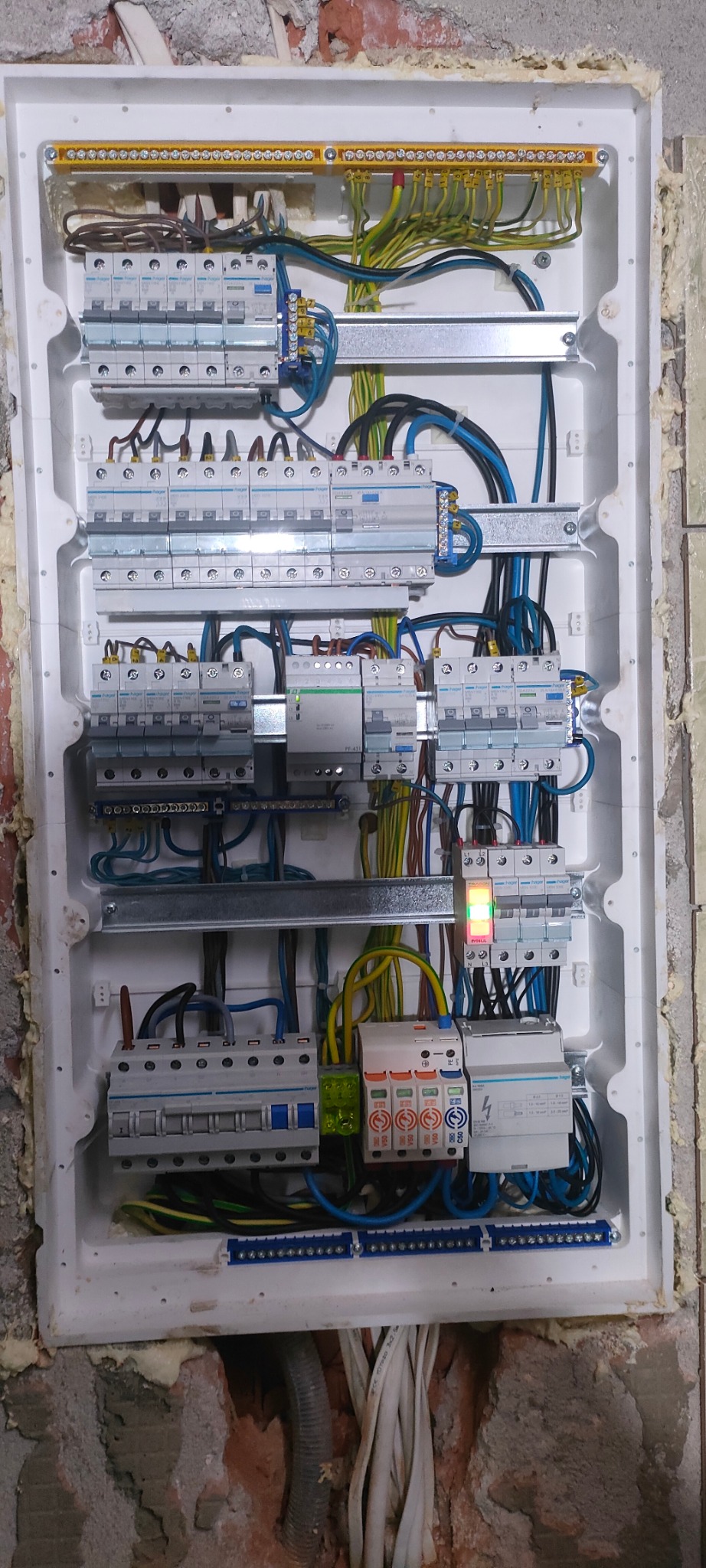 Rozdzielnica elektryczna w trakcie montażu, widoczne zabezpieczenia, przewody i listwy zaciskowe, ściana wokół z widocznymi śladami prac budowlanych.