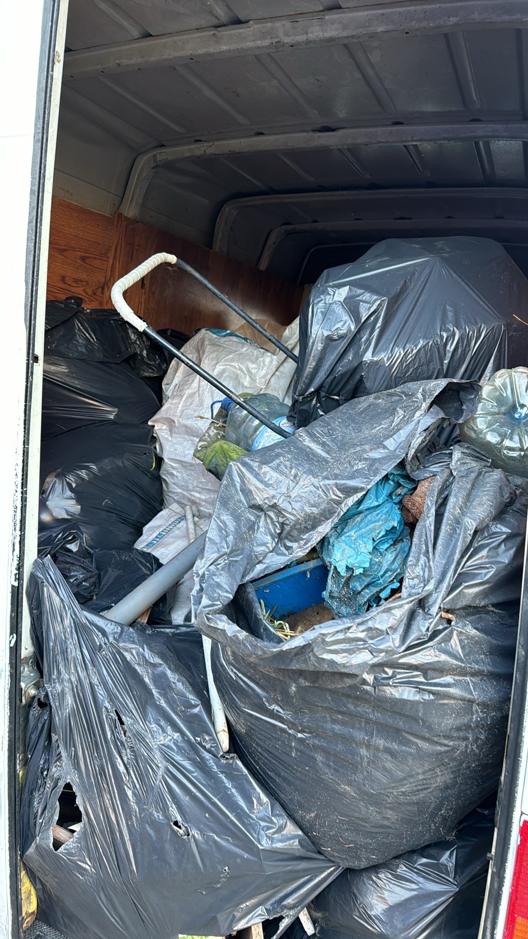 Wnętrze furgonetki wypełnione workami na śmieci, zawierającymi prawdopodobnie odpady budowlane, widoczny fragment wózka transportowego.
