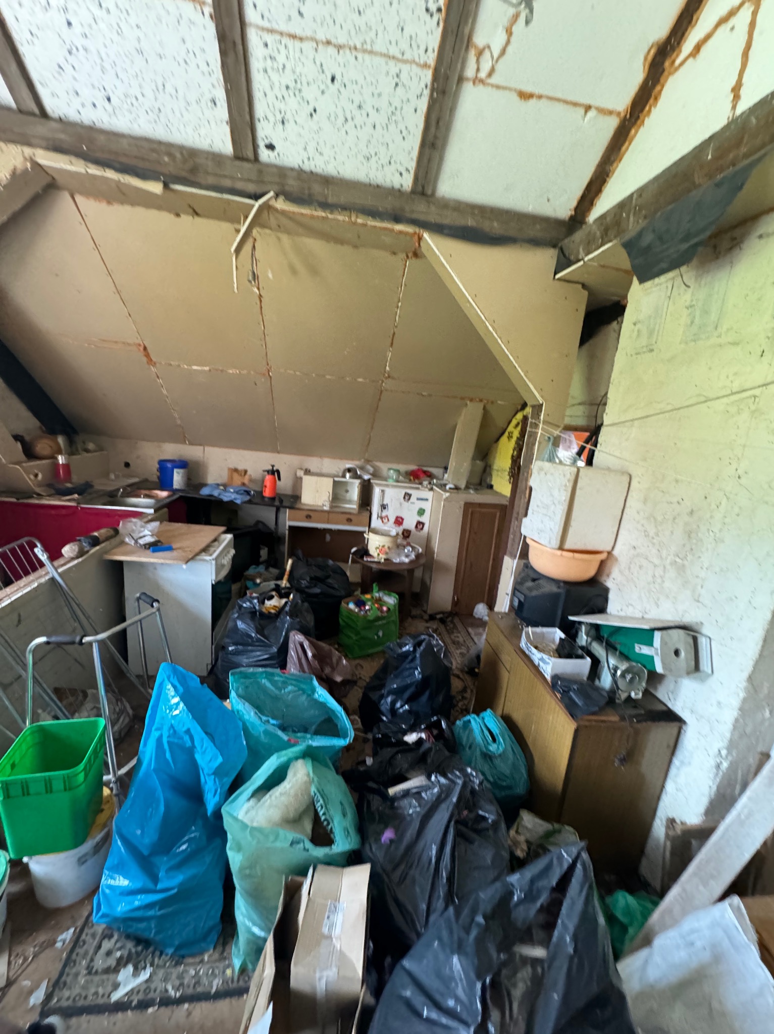 Strych w trakcie opróżniania, wypełniony workami na śmieci, starymi meblami i różnymi przedmiotami przed wywozem, widoczne elementy wyposażenia kuchni i starego budownictwa.