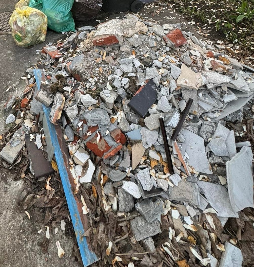 Stos potłuczonego betonu, cegieł i innych resztek budowlanych na betonowej powierzchni z workami na śmieci w tle.