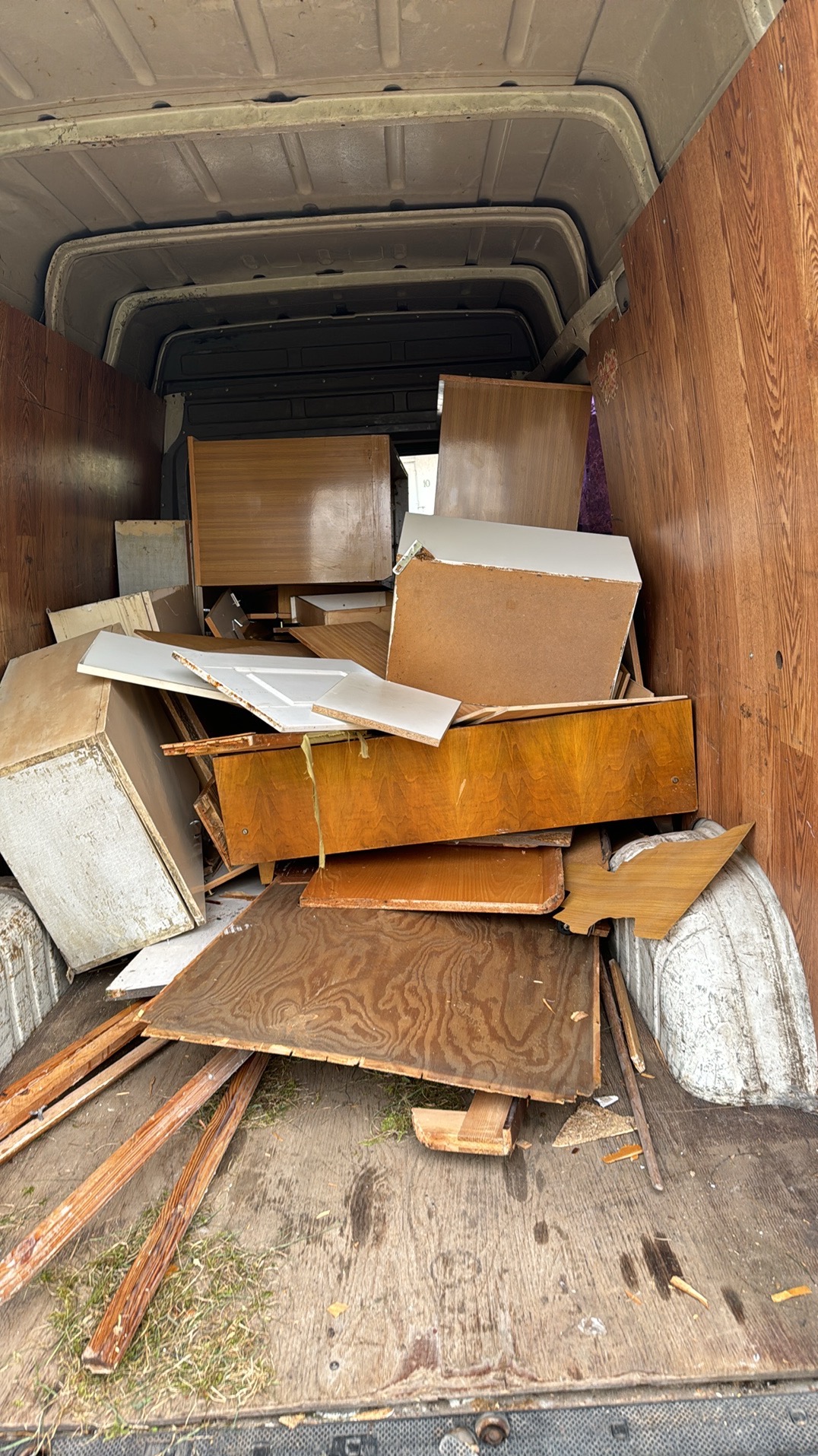 Wnętrze furgonetki załadowane fragmentami mebli, płytami i listwami drewnianymi, pozostałości po demontażu.