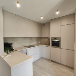 Best Project Sebastian Łobacz - Nowoczesna kuchnia w odcieniach beżu i bieli z drewnopodobną podłogą, oświetleniem punktowym i minimalistycznym wyposażeniem, w tym ekspres do kawy i zlew z baterią.