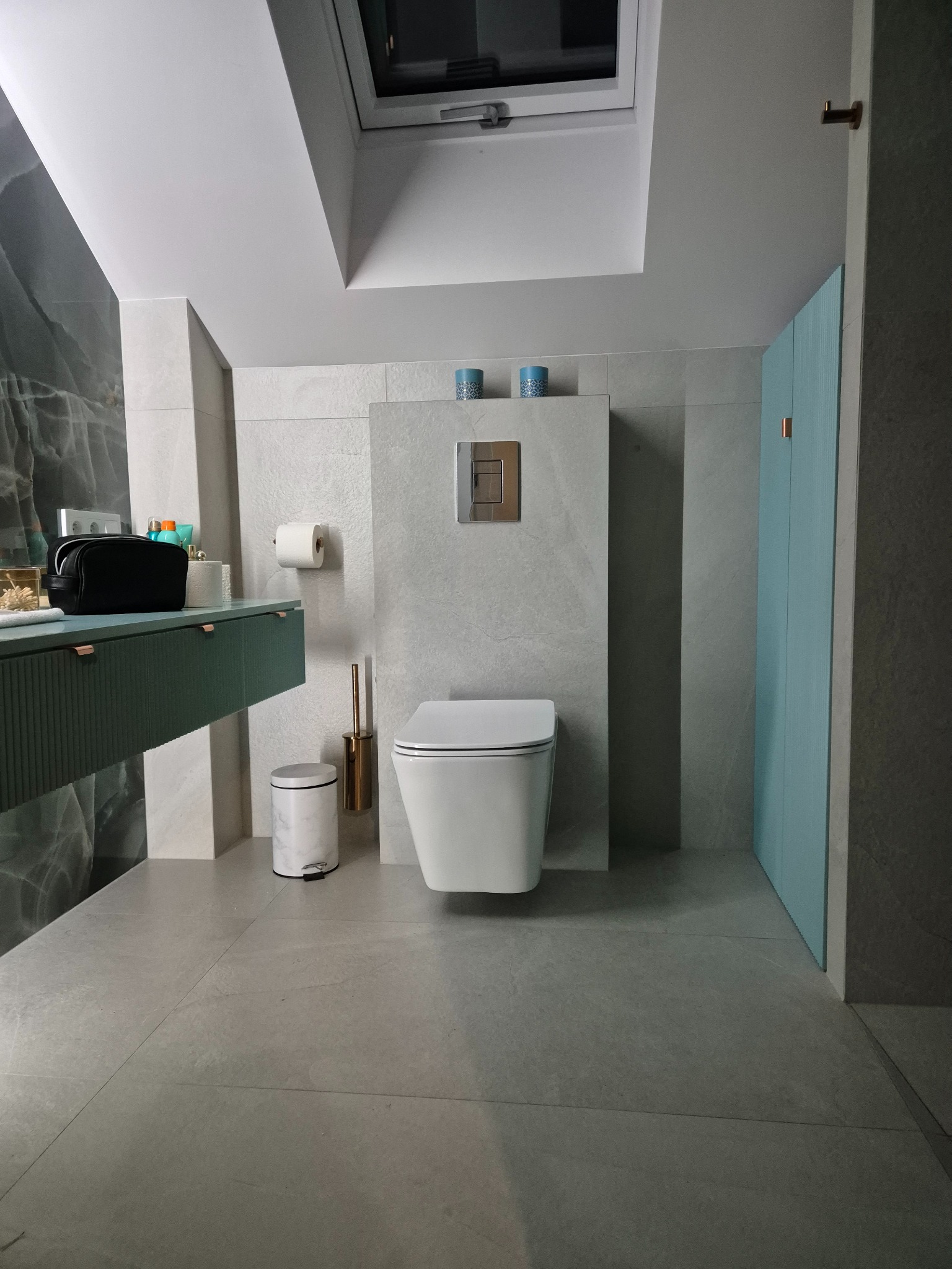 Nowoczesna łazienka z podwieszaną toaletą, szafką umywalkową w kolorze butelkowej zieleni z ryflowanymi frontami i marmurową ścianą akcentującą.