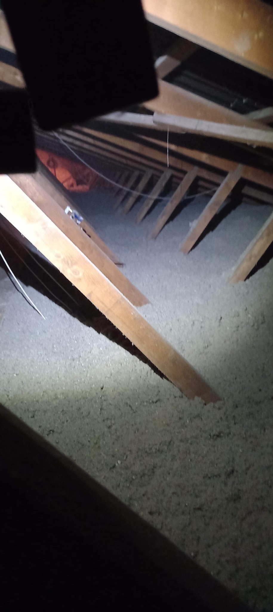 Poddasze z widoczną warstwą izolacji z wełny mineralnej między krokwiami, oświetlone punktowo, z widocznymi przewodami elektrycznymi.