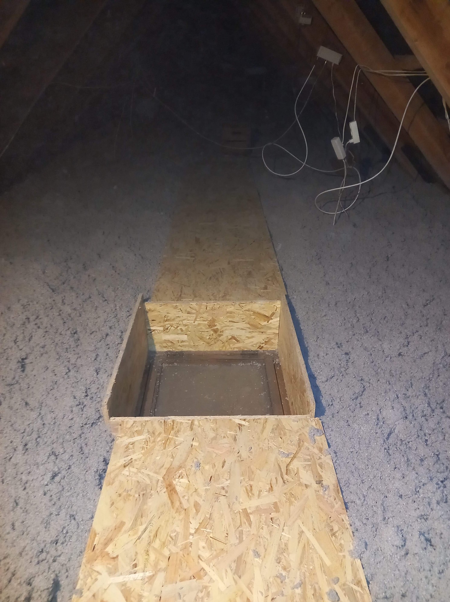 Poddasze z ociepleniem z wełny mineralnej i drewnianą konstrukcją włazu rewizyjnego z płyty OSB, widoczne przewody elektryczne.