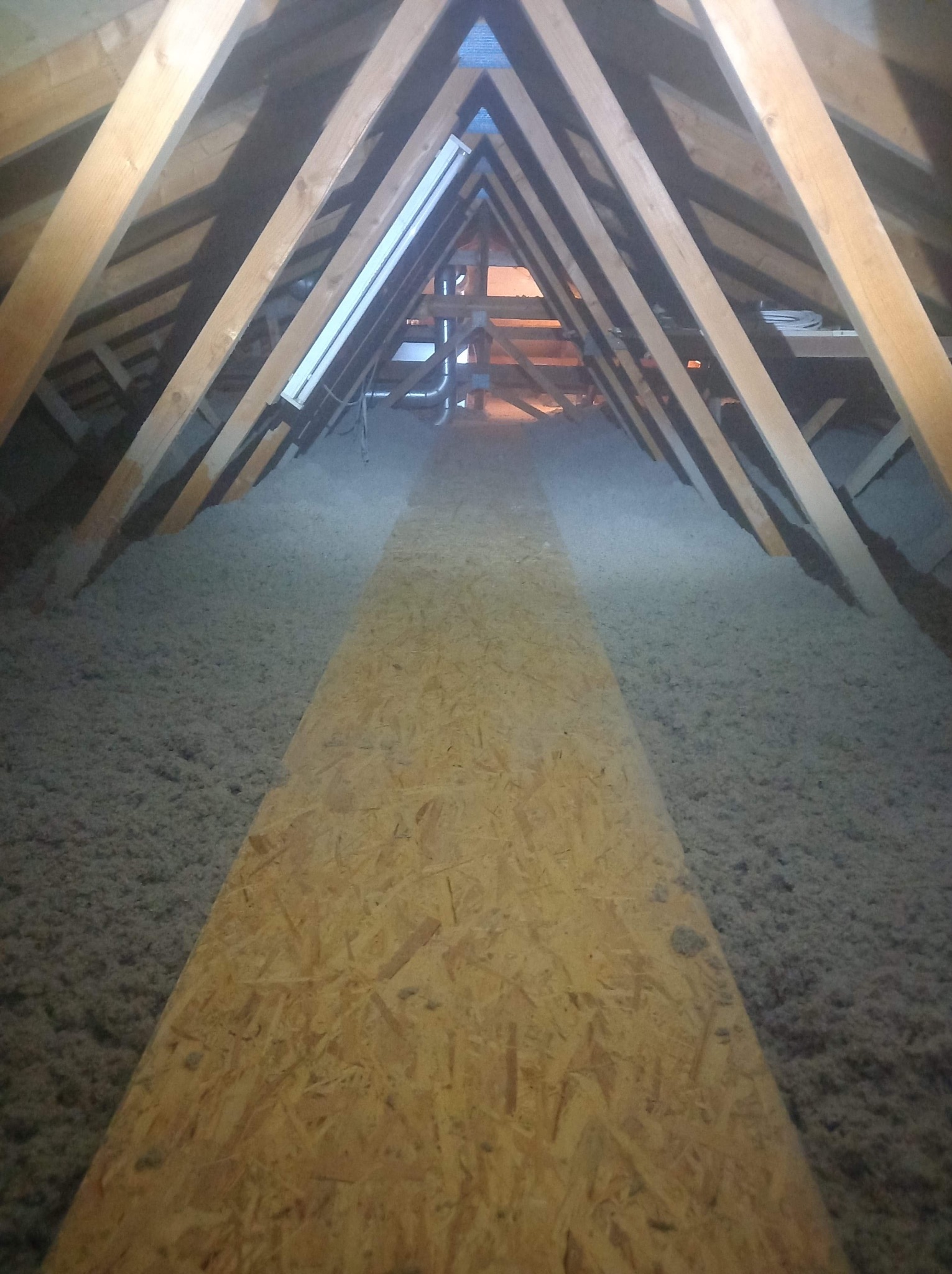 Poddasze ocieplone wełną mineralną z ułożoną ścieżką z płyt OSB, widoczne drewniane krokwie konstrukcji dachu.