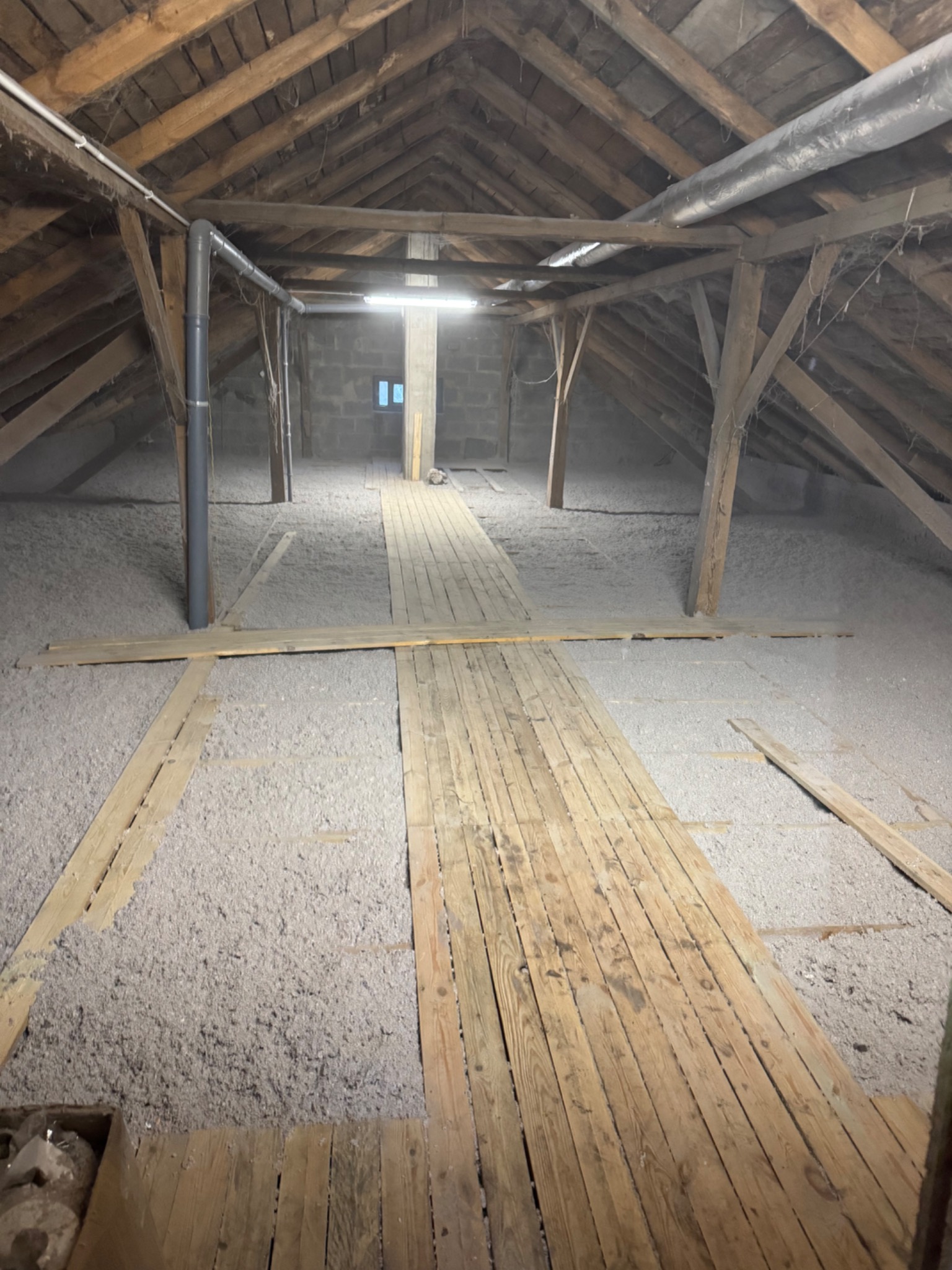 Poddasze z drewnianą konstrukcją, ocieplone szarą wełną mineralną, widoczne deski podłogowe i rury wentylacyjne