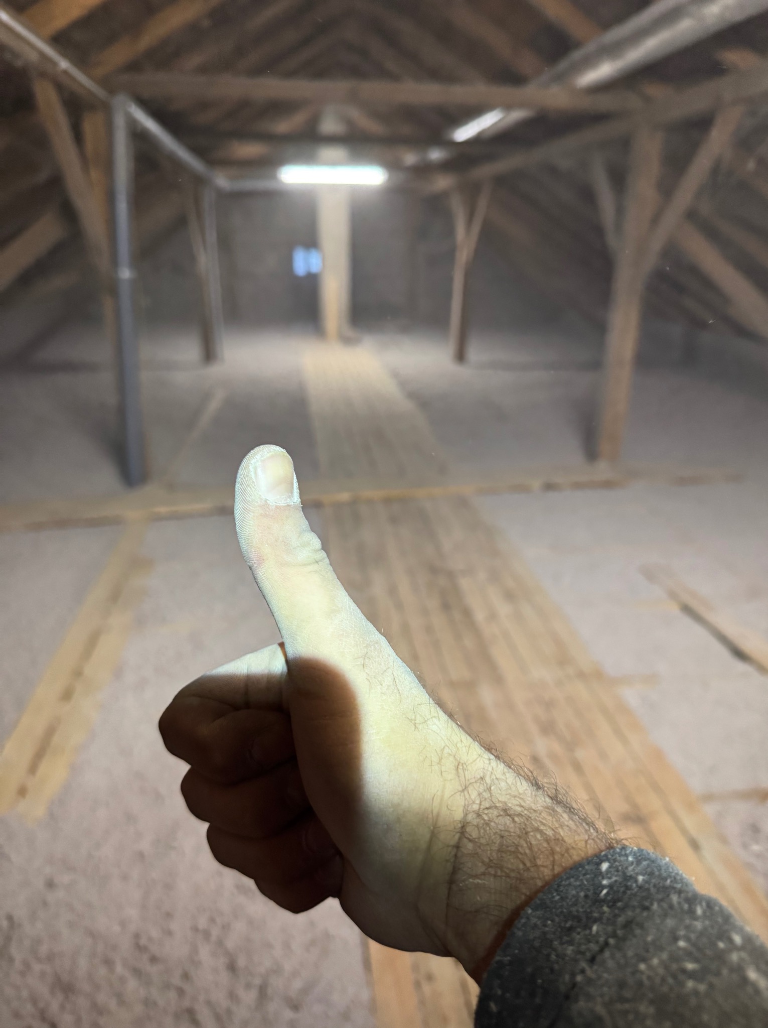 Kciuk w górę, prawdopodobnie po zakończeniu prac na nieocieplonym poddaszu ze starą drewnianą konstrukcją i widocznymi deskami podłogowymi.