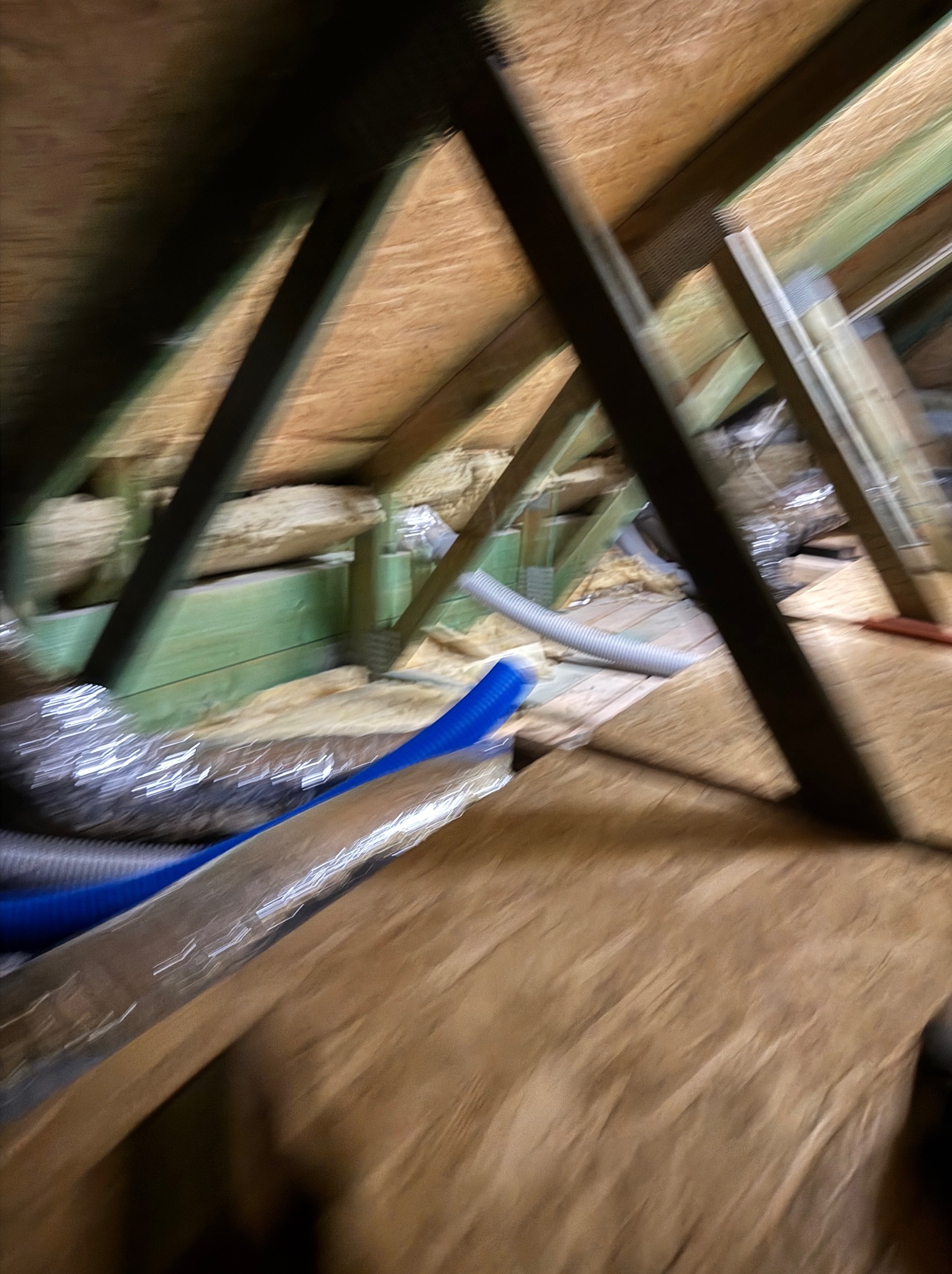 Skośny kadr poddasza z widoczną konstrukcją drewnianą, izolacją i fragmentami instalacji wentylacyjnej. Ujęcie z dołu, podkreślające strukturę dachu.