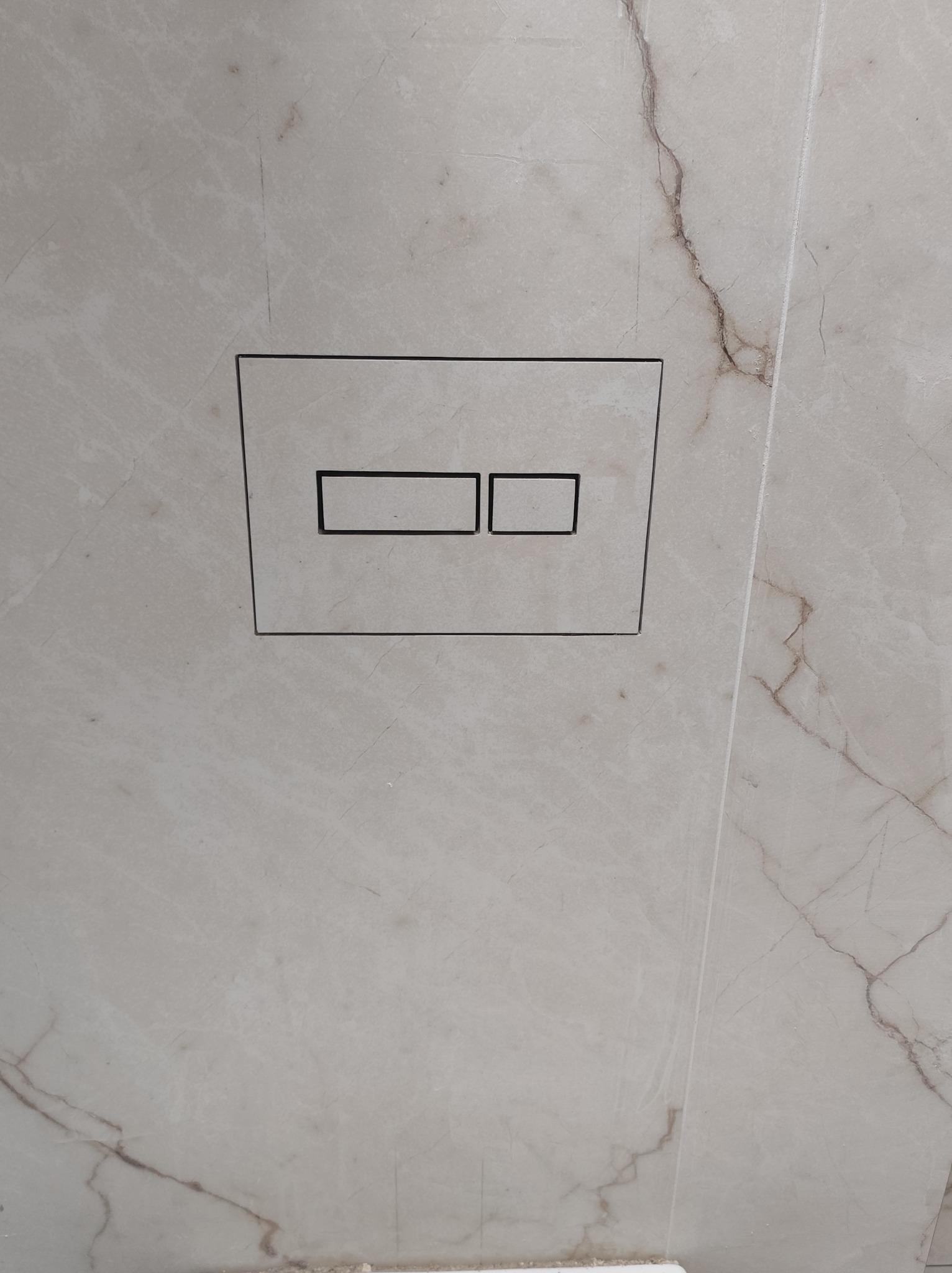 Przycisk spłuczki podtynkowy, dwudzielny, wkomponowany w marmurową ścianę. Minimalistyczny design, precyzyjne wykończenie, widoczne żyłkowanie kamienia.