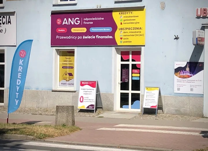 Fasada biura ANG z ofertą kredytów, ubezpieczeń i finansowania biznesu. Widoczny baner reklamowy, flaga z napisem 'Kredyty' i tablice informacyjne.