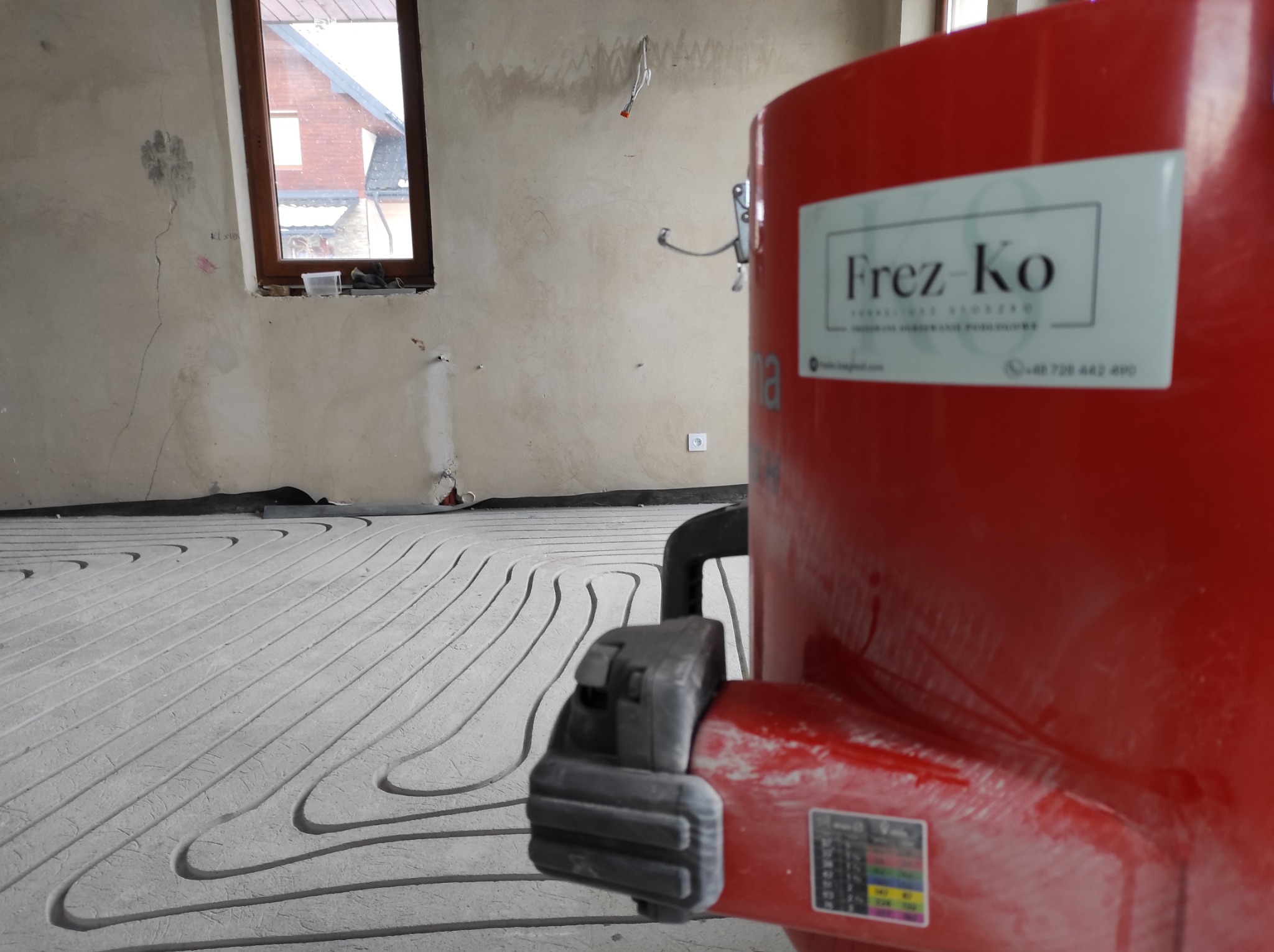 Rozłożone rury ogrzewania podłogowego w trakcie zalewania wylewką w pomieszczeniu w Krzeczowie, widoczna maszyna do wylewania z logo firmy.