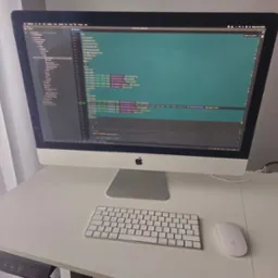 Ekran komputera iMac z widocznym kodem źródłowym na białym biurku w Janczewie, obok klawiatura i myszka Apple.