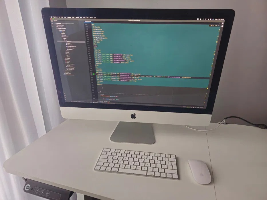 Ekran komputera iMac z widocznym kodem źródłowym na białym biurku w Janczewie, obok klawiatura i myszka Apple.