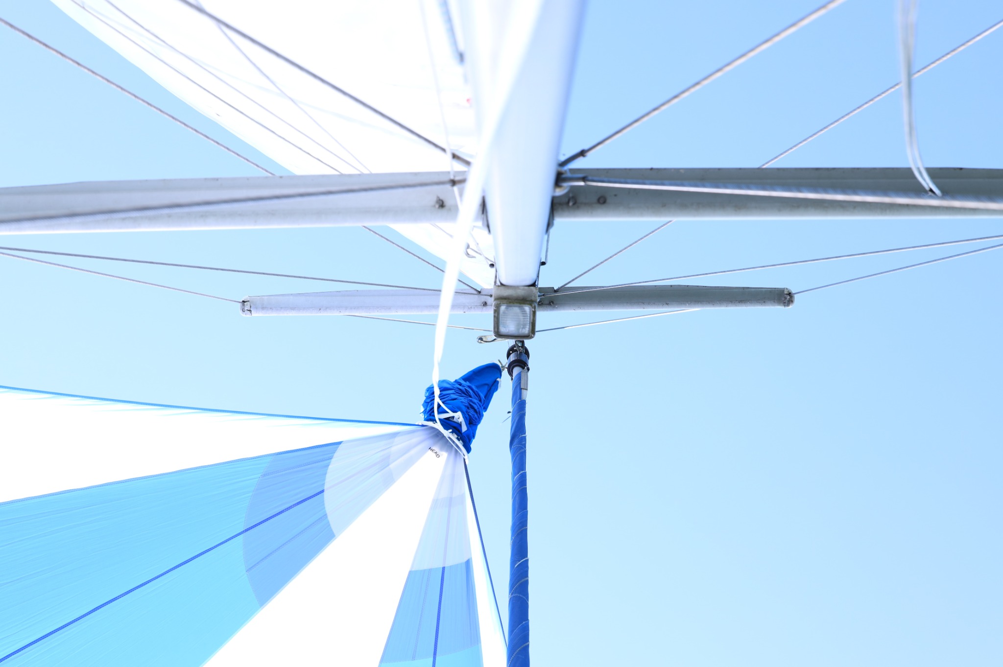 Widok z dołu na maszt i żagiel jachtu na tle błękitnego nieba, z widocznymi linami i elementami konstrukcyjnymi.