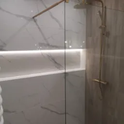 Nowoczesna kabina prysznicowa z marmurowymi płytkami, złotą armaturą i podświetlaną niszą.