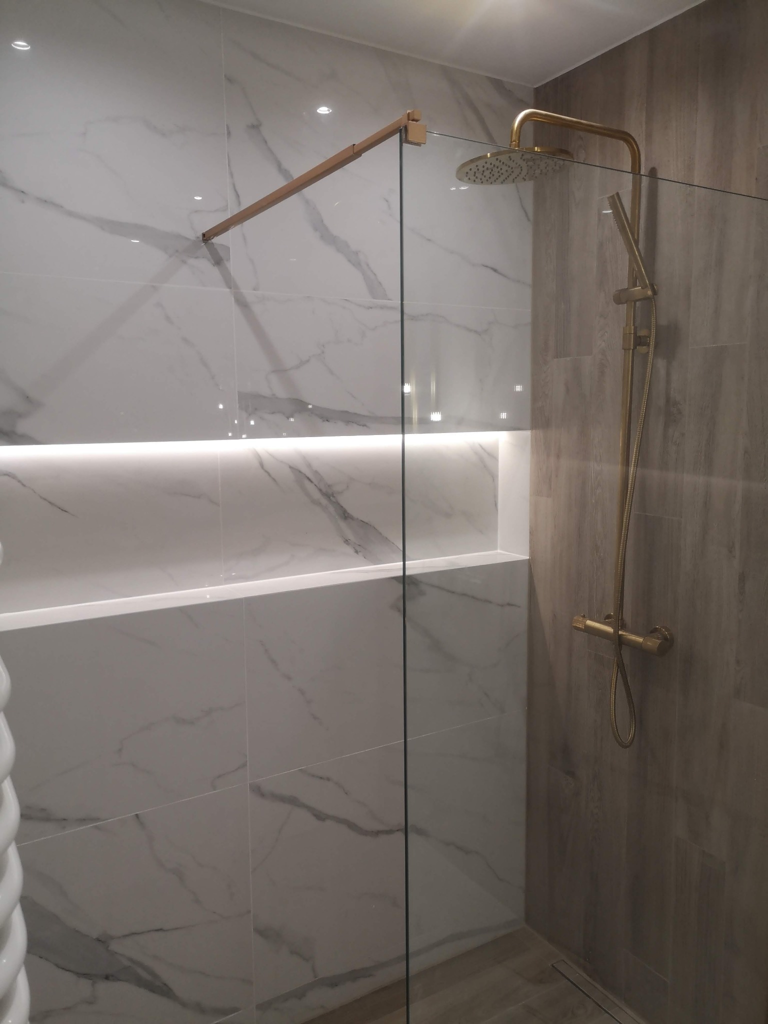 Nowoczesna kabina prysznicowa z marmurowymi płytkami, złotą armaturą i podświetlaną niszą.