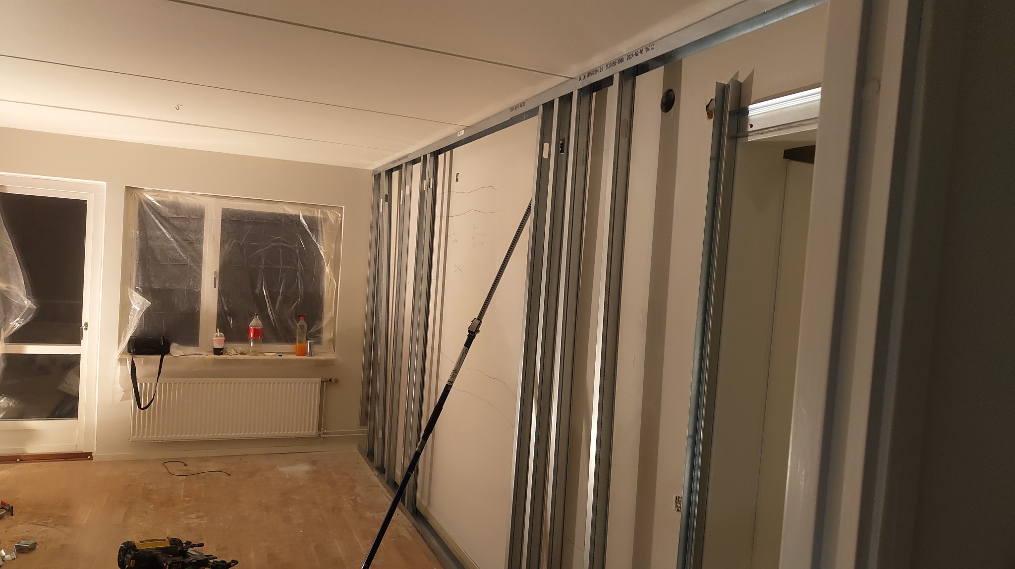 Montaż stelaża z profili metalowych do płyty gipsowo-kartonowej, widoczne narzędzia, okno zabezpieczone folią, pomieszczenie w trakcie remontu.