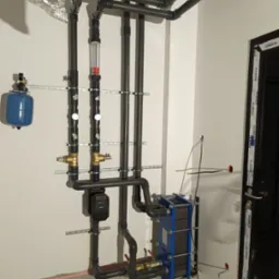 Instalacja wody lodowej z rur PCV, zaworami i wymiennikiem ciepła płytowym w pomieszczeniu technicznym przy ścianie.