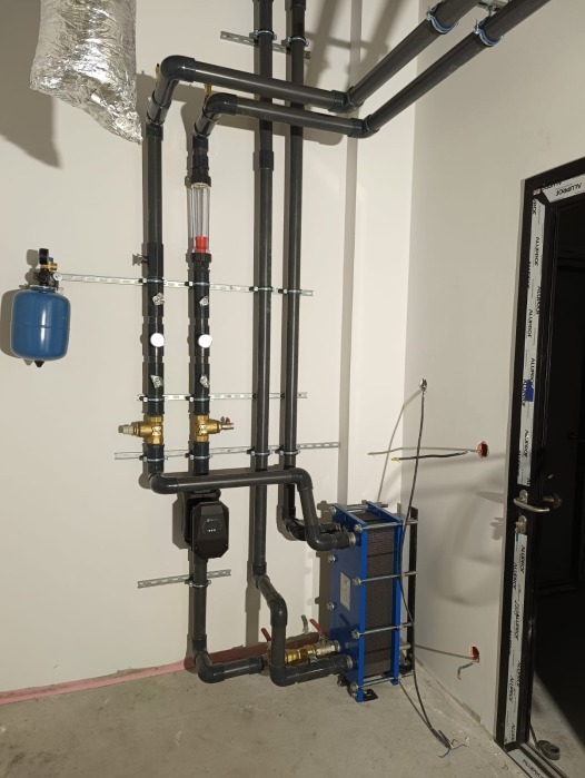 Instalacja wody lodowej z rur PCV, zaworami i wymiennikiem ciepła płytowym w pomieszczeniu technicznym przy ścianie.