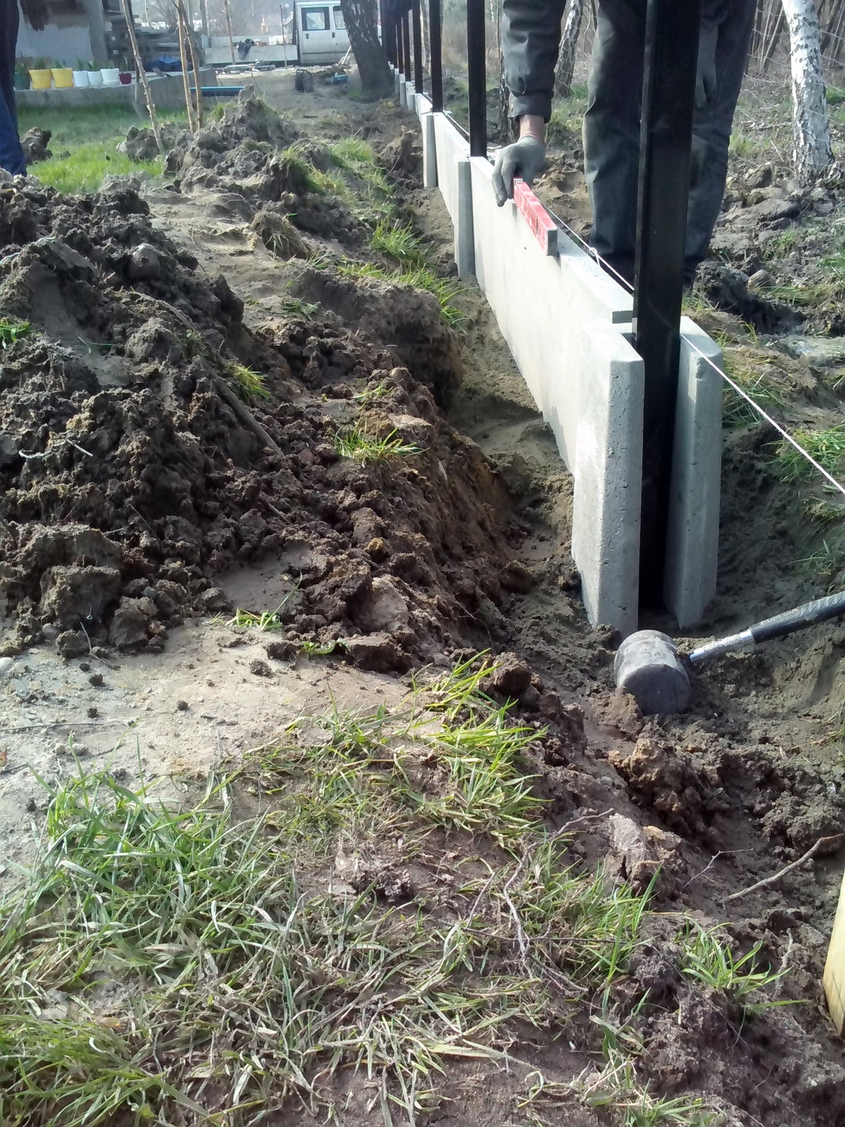 Montaż prefabrykowanej podmurówki ogrodzeniowej z metalowymi słupkami, poziomowana libellą, obok leży gumowy młotek.