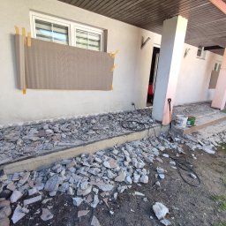 Daniel Fryc Drewniany Danny - Przygotowanie elewacji domu do remontu: fragment ściany z przyklejoną płytą izolacyjną, gruz po skuciu starych płytek tarasowych, widoczne narzędzia i wiaderka z farbą.