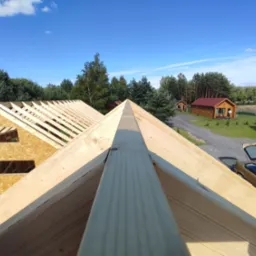 Konstrukcja dachu w trakcie budowy, widok z góry na drewniane krokwie i deskowanie, w tle domki letniskowe i samochód z otwartym bagażnikiem.