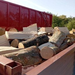 Drewtrans - Ciężarówka z czerwonym kontenerem wypełniona pociętymi kawałkami drewna kominkowego o różnej grubości i fakturze kory, widoczne z bliska pod kątem.
