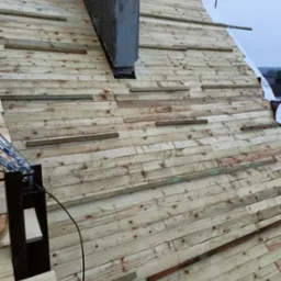 Konstrukcja drewniana dachu w trakcie budowy z widocznym kominem i elementami mocującymi, ujęcie z góry.