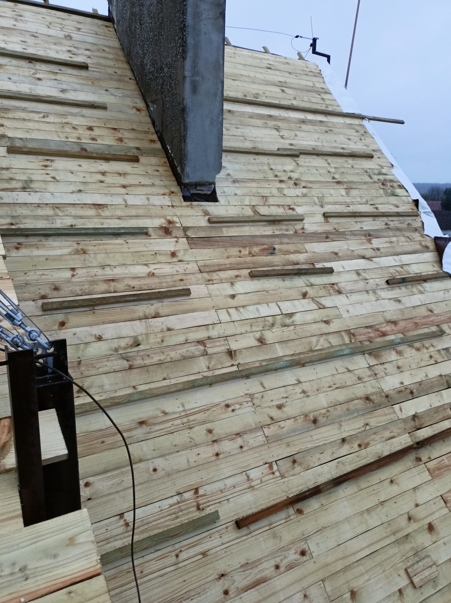 Konstrukcja drewniana dachu w trakcie budowy z widocznym kominem i elementami mocującymi, ujęcie z góry.