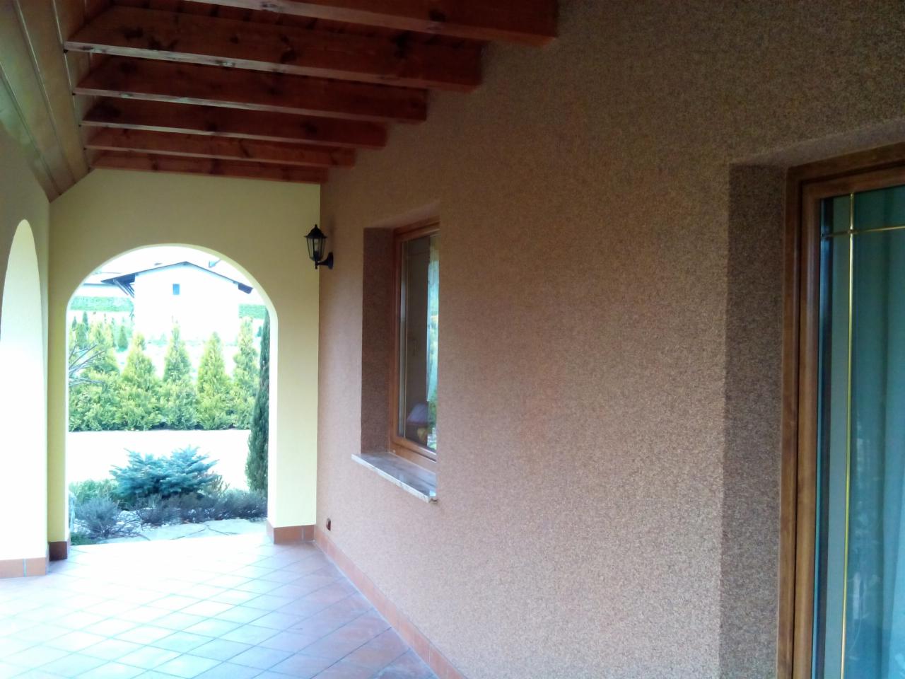 Elewacja zewnętrzna budynku jednorodzinnego w Gostyniu z wykończeniem typu baranek, widok z zadaszonego tarasu z drewnianymi belkami stropowymi.