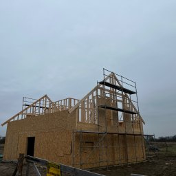 MonterBud - Konstrukcja domu w stanie surowym otwartym z płyt OSB, z widocznym szkieletem dachu i rusztowaniami, pracownik w odblaskowej kamizelce w tle.