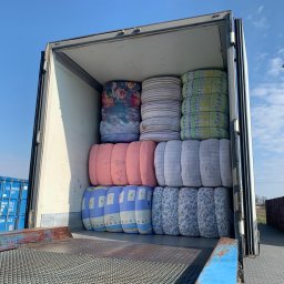 Texland Sp. z o. o. - Wnętrze naczepy wypełnionej sprasowanymi belami tekstyliów w różnych wzorach, widoczne niebieskie kontenery w tle.