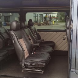 SOMAR MARCIN SOBCZAK - Wnętrze busa z trzema rzędami foteli, czarno-beżowa tapicerka, widok przez otwarte drzwi na zewnątrz w deszczowy dzień.