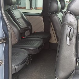 SOMAR MARCIN SOBCZAK - Wnętrze busa z czarnymi skórzanymi siedzeniami, widok z otwartych drzwi na trzy rzędy siedzeń, za oknem budynek stacji benzynowej w deszczowy dzień.